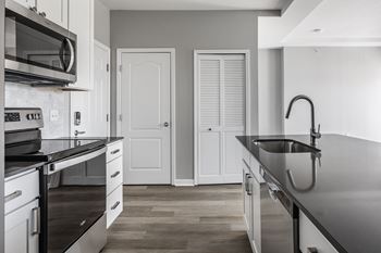 a kitchen with black counter tops and white cabinets and a sink at Alexandria of Carmel Apartments, Carmel, IN